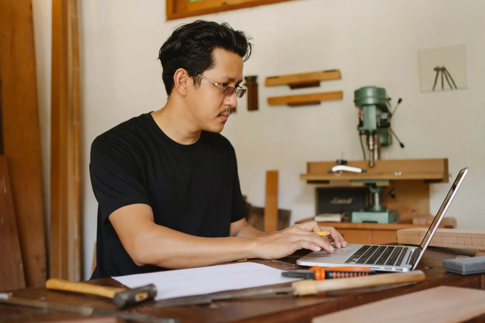 Un artisan menuisier fait une recherche sur son ordinateur portable, à l’établi de son atelier.